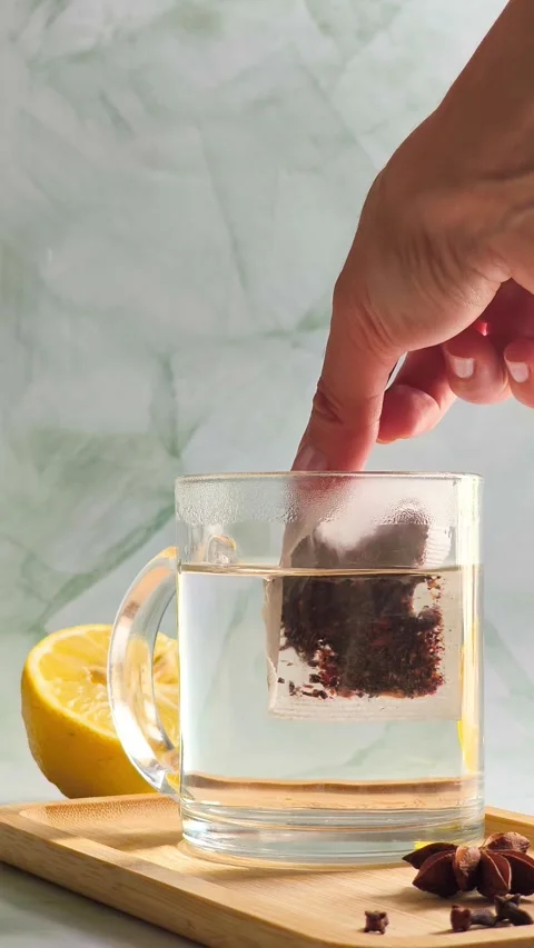 Hand dropping tea bag into clear glass cup with boiling water Stock Footage 336953775
