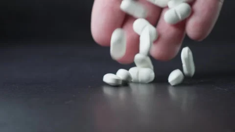 Hand Dropping White Pills on Dark Surface Stock Footage 303512316