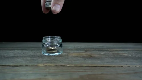 A hand drops coins in slow motion into a jar. Stock Footage 197016024
