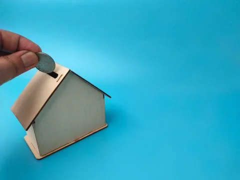 A hand drops a single silver coin into the roof slot of a miniature wooden .. Stock Photos