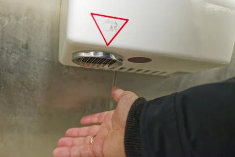 Hand drying with automatic electric hand dryer in public restroom Stock Photos