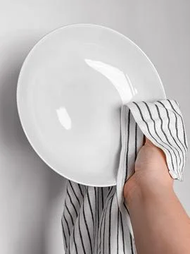 Hand drying white ceramic plate with striped cloth in kitchen setting Stock-Fotos