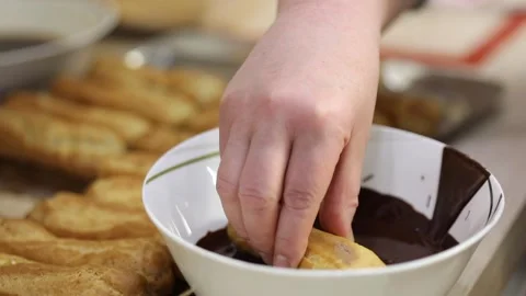 Hand dunks eclair into chocolate, close up, slow motion Video stock 276364167