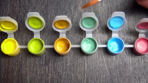 The hand dunks an orange artificial brush in green acrylic paint. Stock Footage 128758252