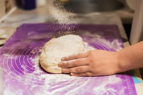 A hand dusting a portion of raw dough with a cloud of flour on a bright pur.. Stock Photos