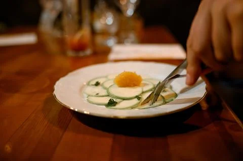 A hand eats an appetizer of thin slices of zucchini with caviar on a white pl Stock Photos