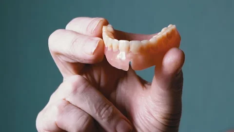Hand Elderly Holding a Removable Upper Jaw Denture on a Blurred Background Stock Footage 235701319
