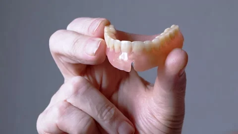 Hand Elderly Holding a Removable Upper Jaw Denture on a Blurred Background Stock Footage 236187506