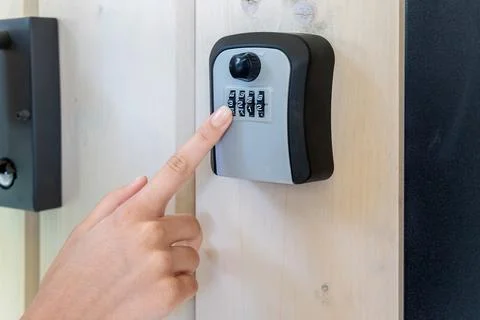 Hand Entering Code on Wall-Mounted Lockbox. Close-up of a person entering a Stock Photos