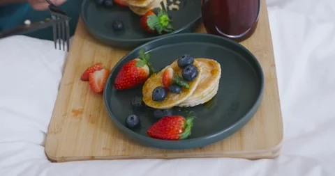 Hand entering from left is cutting pancakes with knife and fork, preparing bite Stock Footage 344402194