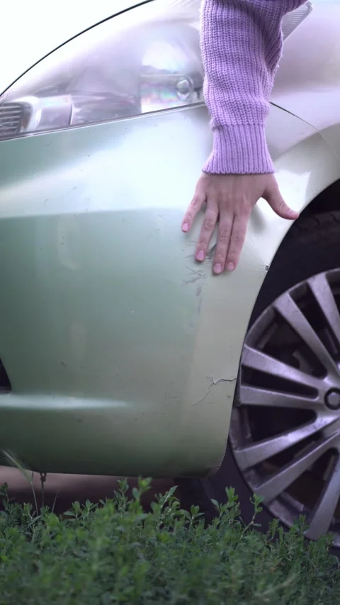 Hand examines scratches and cracks on a light green car bumper after an accident Video stock 342442523
