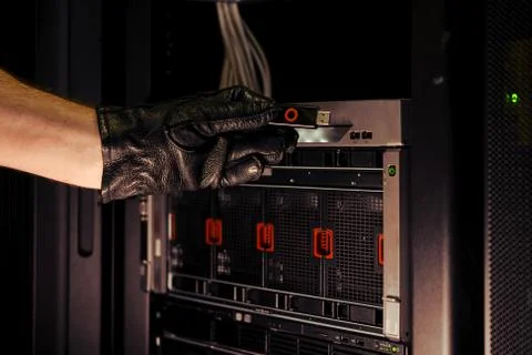 Hand with a flash drive from a hacking device at the server. Concept of data  Stock Photos