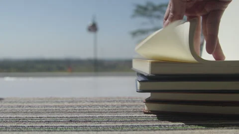 Hand Flipping Pages of a Stack of Notebooks by a Sunny Window Stock Footage 339195509