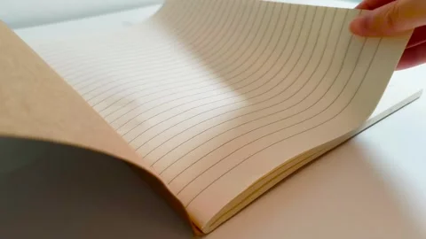 Hand flipping through a notebook, turning white lined paper pages on desk table 動画素材 317135398