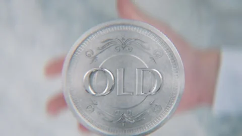 A hand flips a coin marked New and Old, spinning toward the camera in slow .. Stock Footage 296366839