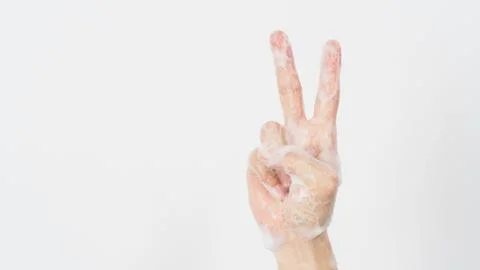 Hand with foam soap bubble is doing Victory or Peace hand Sign on white backg Stock Photos