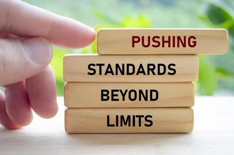 Hand forcefully advances blocks reading PUSHING STANDARDS BEYOND LIMITS, pr.. Stock Photos