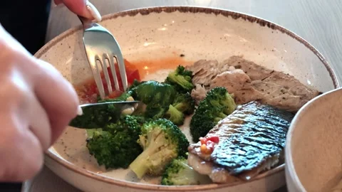 Hand with fork adjusts fresh herb garnish above fish fillet in creamy sauce Stock Footage 343514565
