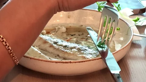 Hand with fork adjusts fresh herb garnish above fish fillet in creamy sauce 스톡 동영상 343515334
