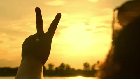 A hand forms the V-sign against a golden sky. Video stock 315750660
