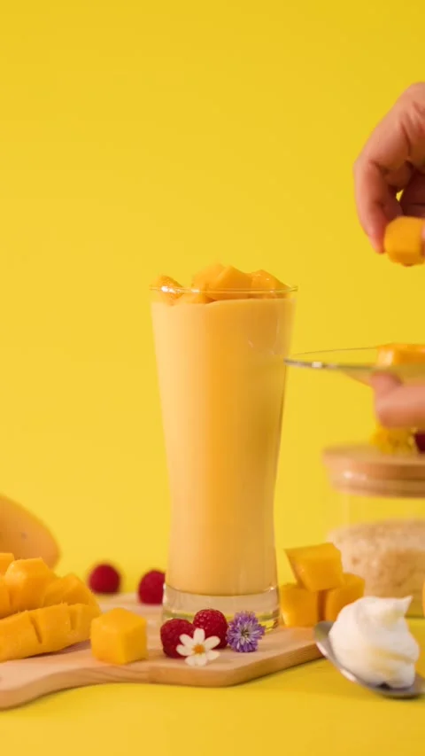 Hand Garnishing Mango Smoothie with Fresh Fruit Cubes Stock Footage 323679765