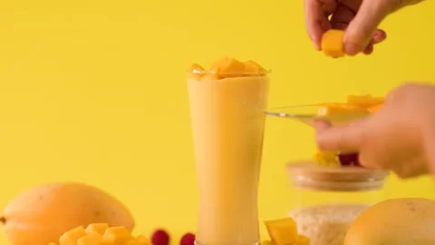 Hand Garnishing Mango Smoothie with Fresh Fruit Cubes Stock Footage 323891680