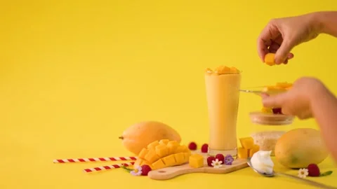 Hand Garnishing Mango Smoothie with Fresh Tropical Fruit Cubes Stock Footage 323891710