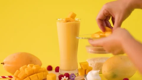 Hand Garnishing Mango Smoothie with Fresh Tropical Fruit Cubes Stock Footage 323891903