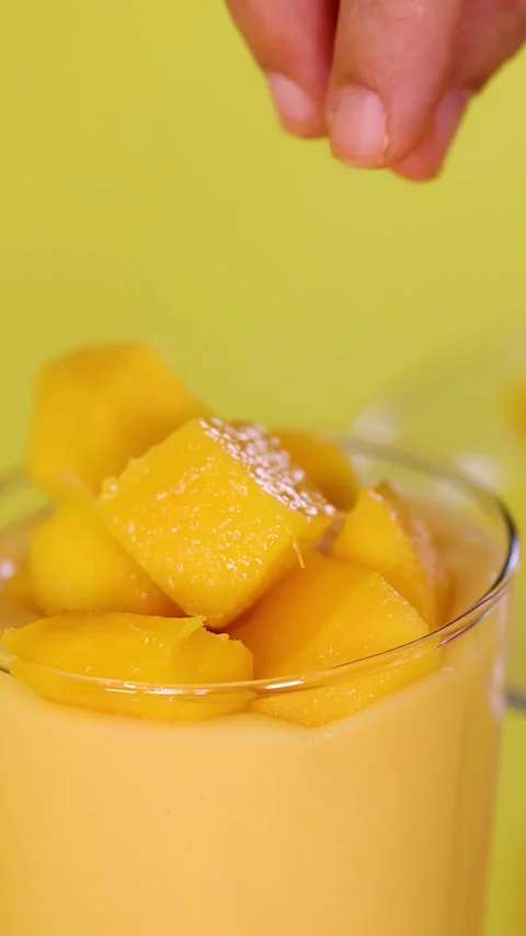 Hand Garnishing Mango Smoothie with Fresh Fruit Cubes Stock Footage 324688513