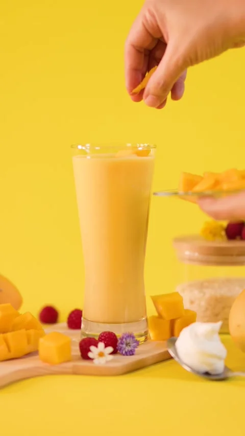 Hand Garnishing Mango Smoothie with Fresh Fruit Cubes Stock Footage 324938367