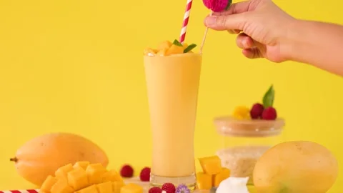 Hand Garnishing Mango Smoothie with Raspberry on Yellow Background Stock Footage 325692761