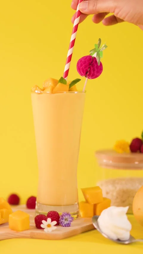Hand Garnishing Mango Smoothie with Straw on Yellow Background Stock Footage 324351844