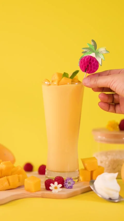 Hand Garnishing Mango Smoothie with Tropical Drink Stirrer Stock Footage 324351397