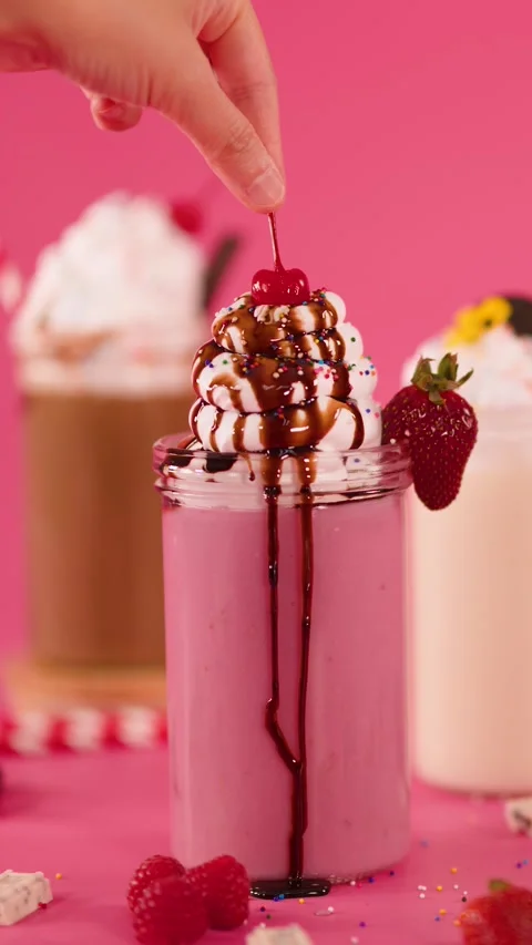 Hand Garnishing Strawberry Milkshake with Cherry and Chocolate Drizzle Stock Footage 321325413