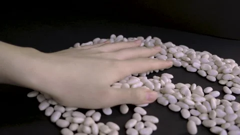 Hand gathering white beans into pile on black background 4k 10bit 120fps Stockbeeldmateriaal 332718608