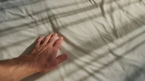 Hand gently caresses bedsheet as sunlight shines into room through window Stock Footage 339058558