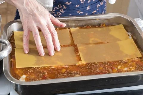 Hand gently places lasagna sheets atop sauce in baking tray Stock Photos