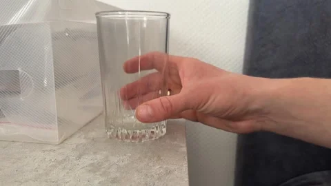 A hand gently pushes a transparent drinking glass across a smooth surface Stock Footage 335074489
