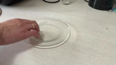A hand gently slides a clear glass plate across a white table surface 動画素材 335073897