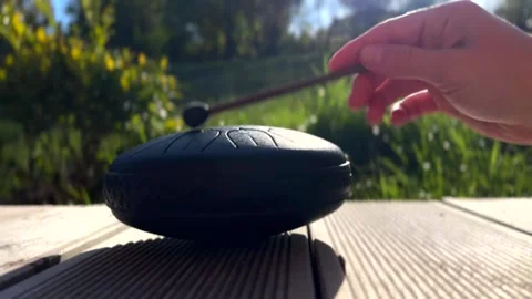 Hand gently strikes black handpan in peaceful garden filled with greenery 動画素材 340382431