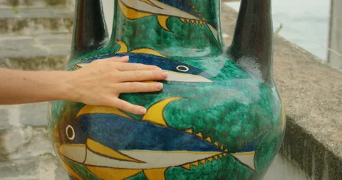 Hand gently touching ceramic vase with fish painting on Italian coastal steps Stock Footage 305396722