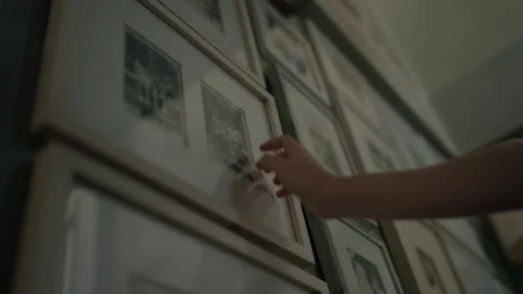 A hand gently touching old framed asian family photographs on the wall, Memories Stock Footage 328491516