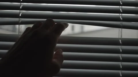 Hand gets close to shut window blinds and crack opens one to peek outside room Stock Footage 257792809