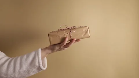 Hand with a gift box on a beige background, Christmas surprise, festive wra.. Stock Footage 257331460