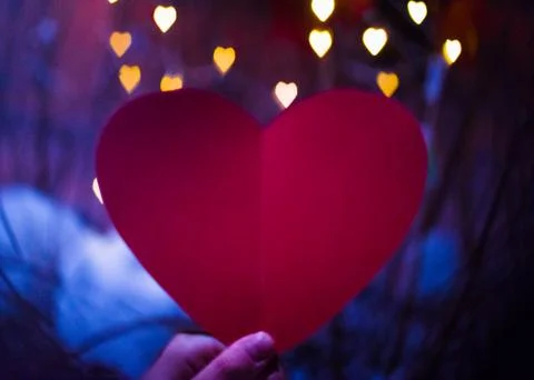 Hand of a girl holding paper red heart, heart bokeh Stock Photos