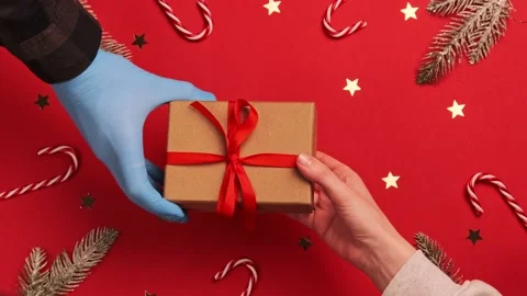 Hand gives gift box in protective gloves  COVID 19. Christmas 2021. Pandemic Stock Footage 144136938