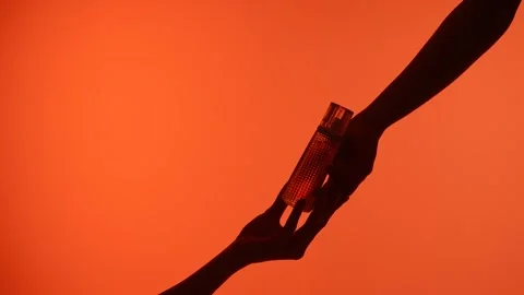 Hand Giving Perfume Bottle in Orange Background Silhouette Stock-Footage 313525778