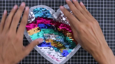 Hand glides over a heart-shaped reversible sequin patch with colorful Video stock 280532565