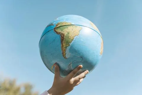Hand with a globe on a clear sky background. Children's hand with earth plane Stock Photos