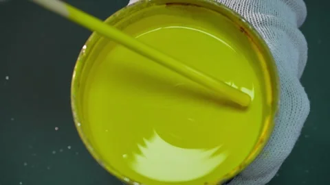 Hand gloved painter mixing yellow paint in metal paint can with wooden stick Vídeos de archivo 293954083
